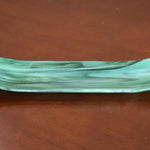 Green and seafoam fused glass channel tray on a brown tabletop, showing marbled swirls and subtle bubbles.