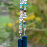 Brightly colored glass beads from Ghana, South Africa&#39;s Krobo tribe are strung with large solid clear glass beads, hanging vertically against blurred background. The two strung &quot;legs&quot; are anchored by two pieces of dark aqua blue fused glass.