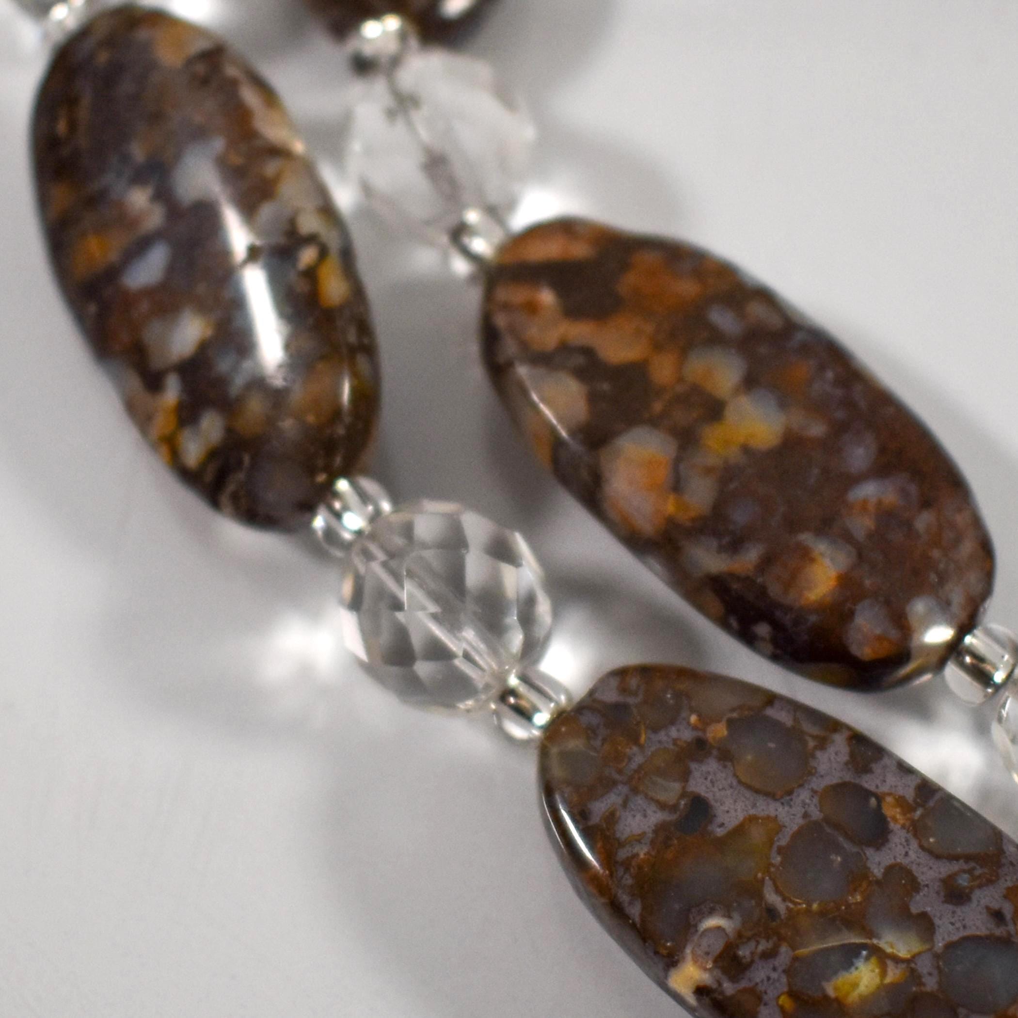 Close up of three oval-shaped fire opal stone beads with faceted clear glass crystal beads in between the stone beads, laying on a white surface.