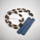 A decorative wind chime with a string of oval-shaped, brown and blue beads interspersed with clear, round beads coiled on a white surface.