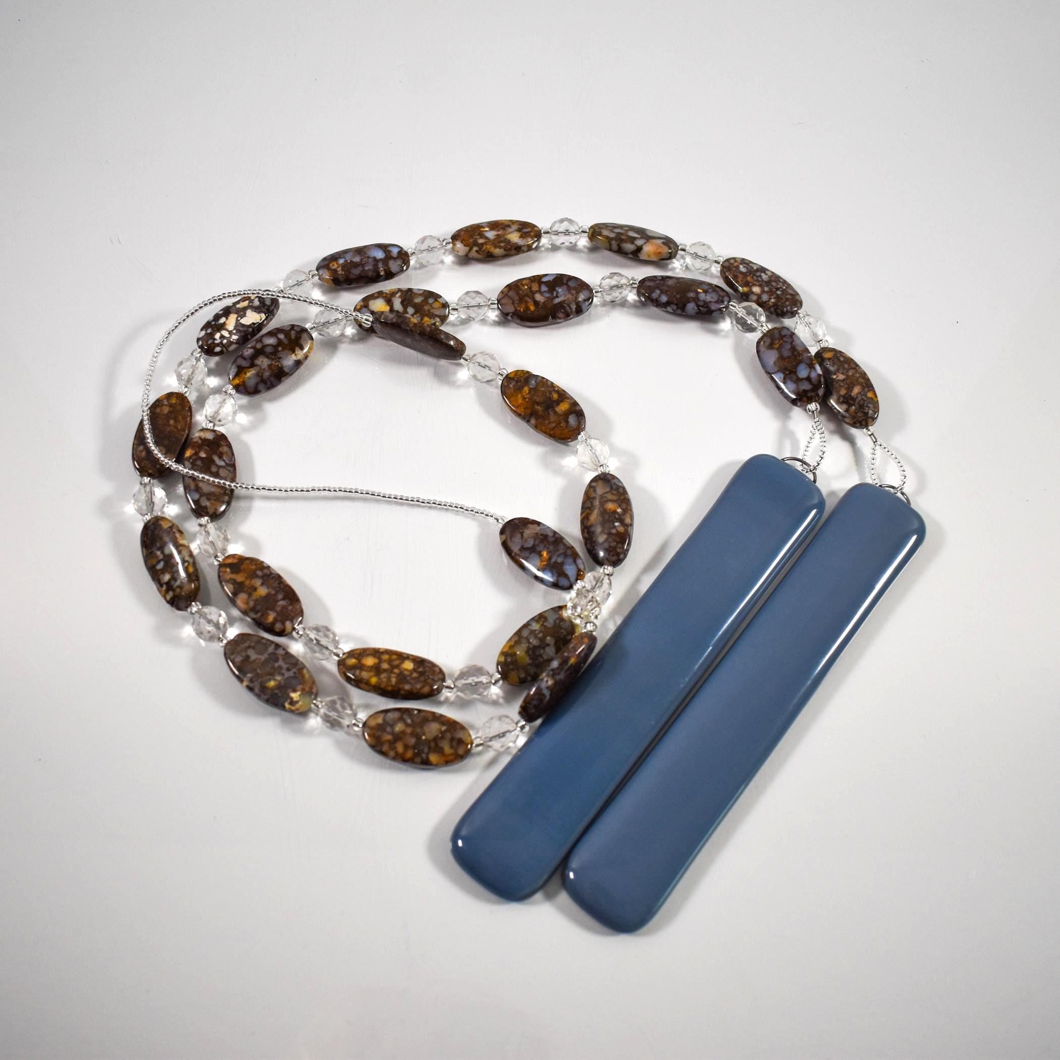 A decorative wind chime with a string of oval-shaped, brown and blue beads interspersed with clear, round beads coiled on a white surface.