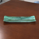 Green and seafoam fused glass channel tray on a brown tabletop, showing marbled swirls and subtle bubbles.