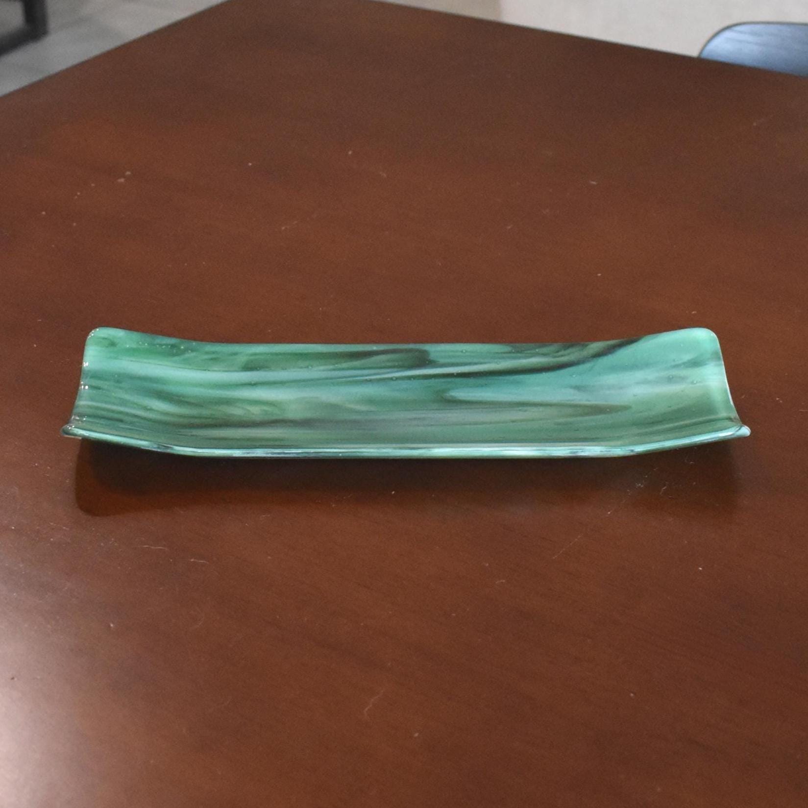 Green and seafoam fused glass channel tray on a brown tabletop, showing marbled swirls and subtle bubbles.
