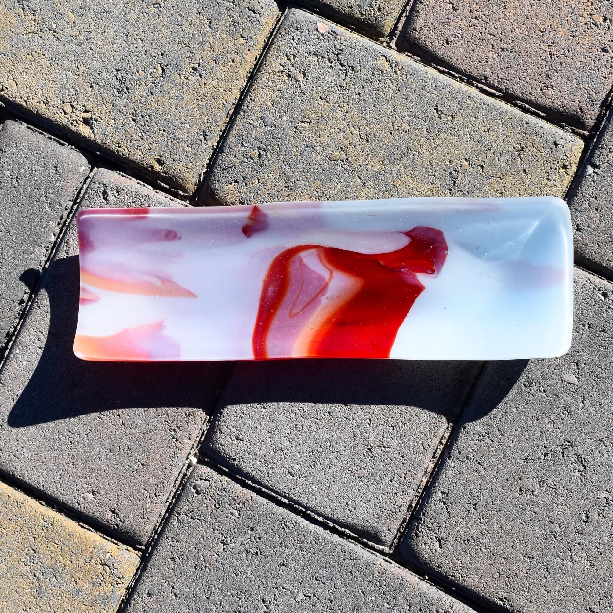 Top-down view of the rectangular fused glass tray on stone pavers, with a bold red “flame” shape in the center.