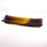 Angled view of the rectangular glass channel tray on a white background, blending transparent amber with deep purple corners.