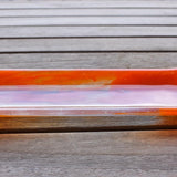 Orange and clear fused glass channel tray photographed from the side on a slatted wood table.