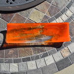 Orange and clear fused glass channel tray photographed from above on a stone tile table in sunlight.