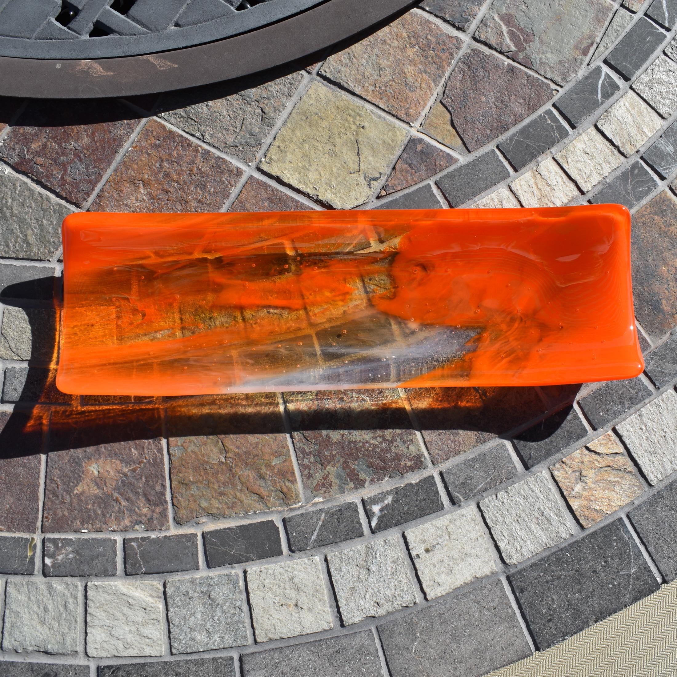 Orange and clear fused glass channel tray photographed from above on a stone tile table in sunlight.