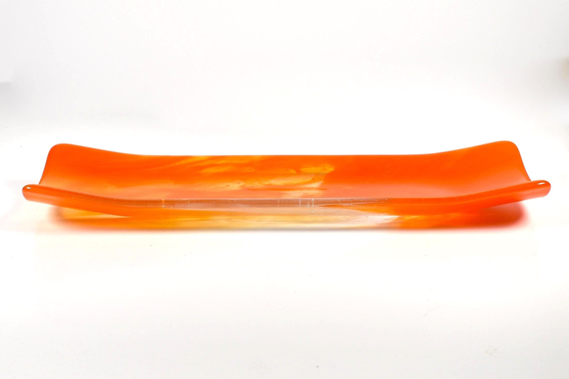 Orange and clear fused glass channel tray photographed from the side on a white background, with soft amber swirls in the center.