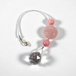 Large round carved rose quartz bead flanked by two smaller pink stone beads and anchored by round crystal prism, on white surface.