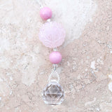 Large round carved rose quartz bead flanked by two smaller pink stone beads and anchored by round crystal prism, on marbled tile surface.
