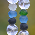 Six recycled glass round beads, strung on two hanging wires and separated by large clear glass beads. The recycled glass beads are from the Krobo tribe in Ghana, Africa and are blue, green, black and white.