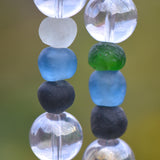 Six recycled glass round beads, strung on two hanging wires and separated by large clear glass beads. The recycled glass beads are from the Krobo tribe in Ghana, Africa and are blue, green, black and white.