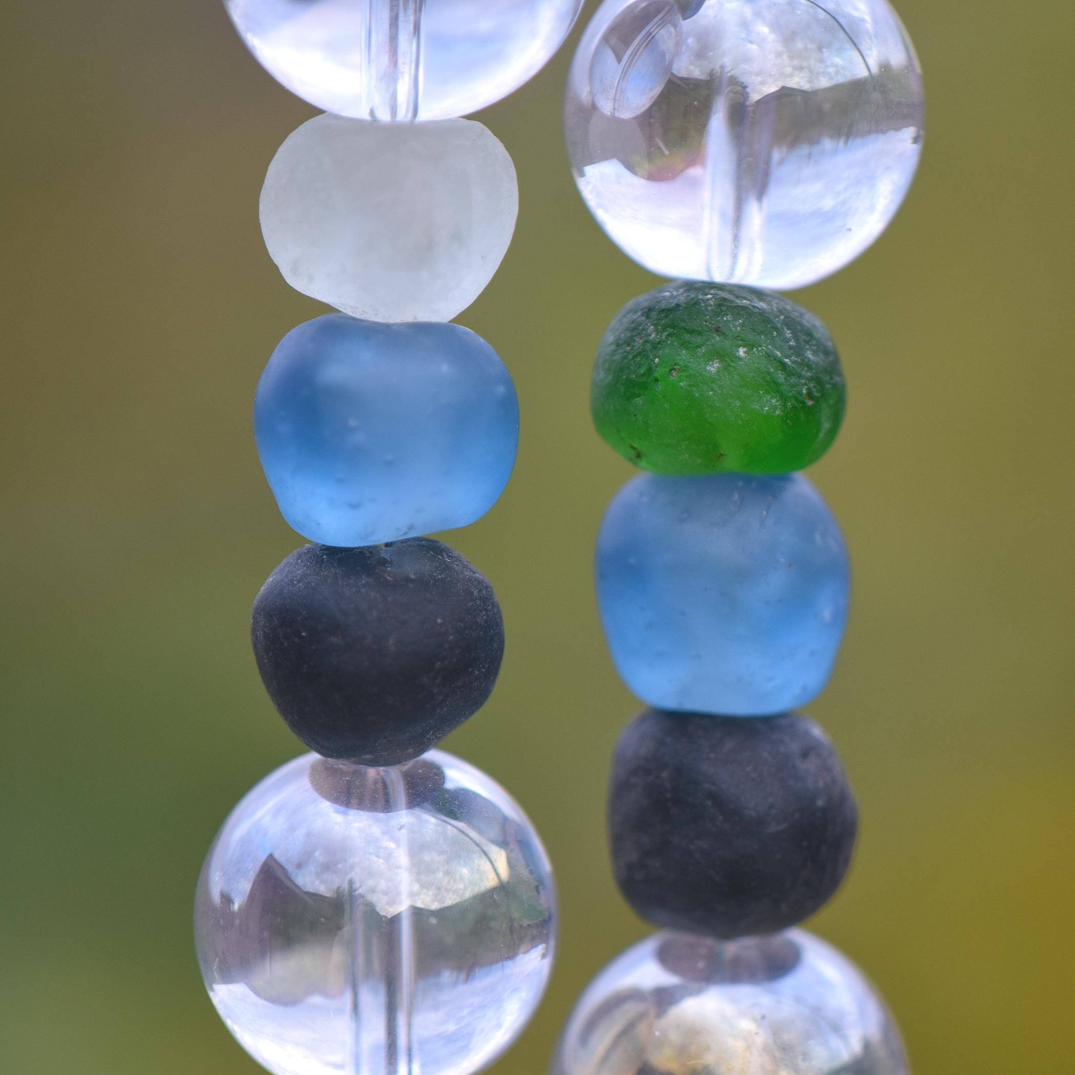 Six recycled glass round beads, strung on two hanging wires and separated by large clear glass beads. The recycled glass beads are from the Krobo tribe in Ghana, Africa and are blue, green, black and white.