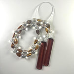 Cinjo Handmade wind chime coiled on a white surface, clearly showing the beaded wire and the two piece of fused glass in pale purple. The Rhyolite stone beads are tear drop shaped and there is a larger, clear, reflective glass bead in between each stone bead. The stone beads are marked and in shades of brown, tan and gray. Any wire not covered by larger beads are covered with silver-lined seed beads.