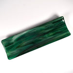 Top angled view of a long emerald green fused glass tray with smoky swirls and softly raised edges on white.