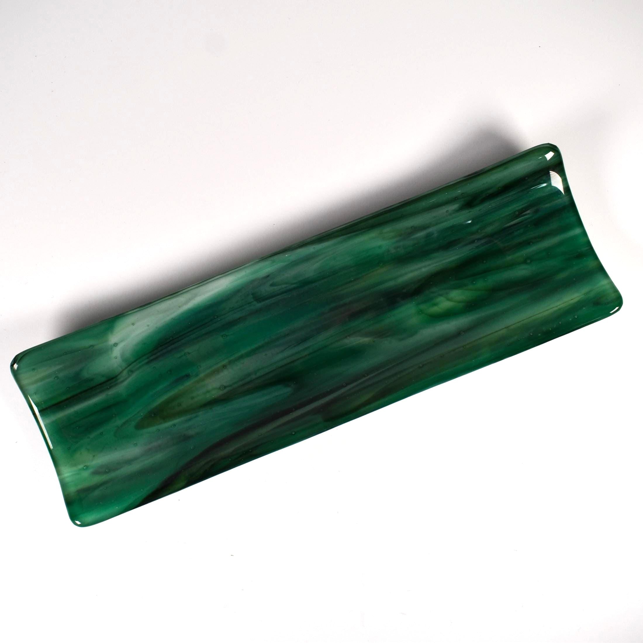 Top angled view of a long emerald green fused glass tray with smoky swirls and softly raised edges on white.