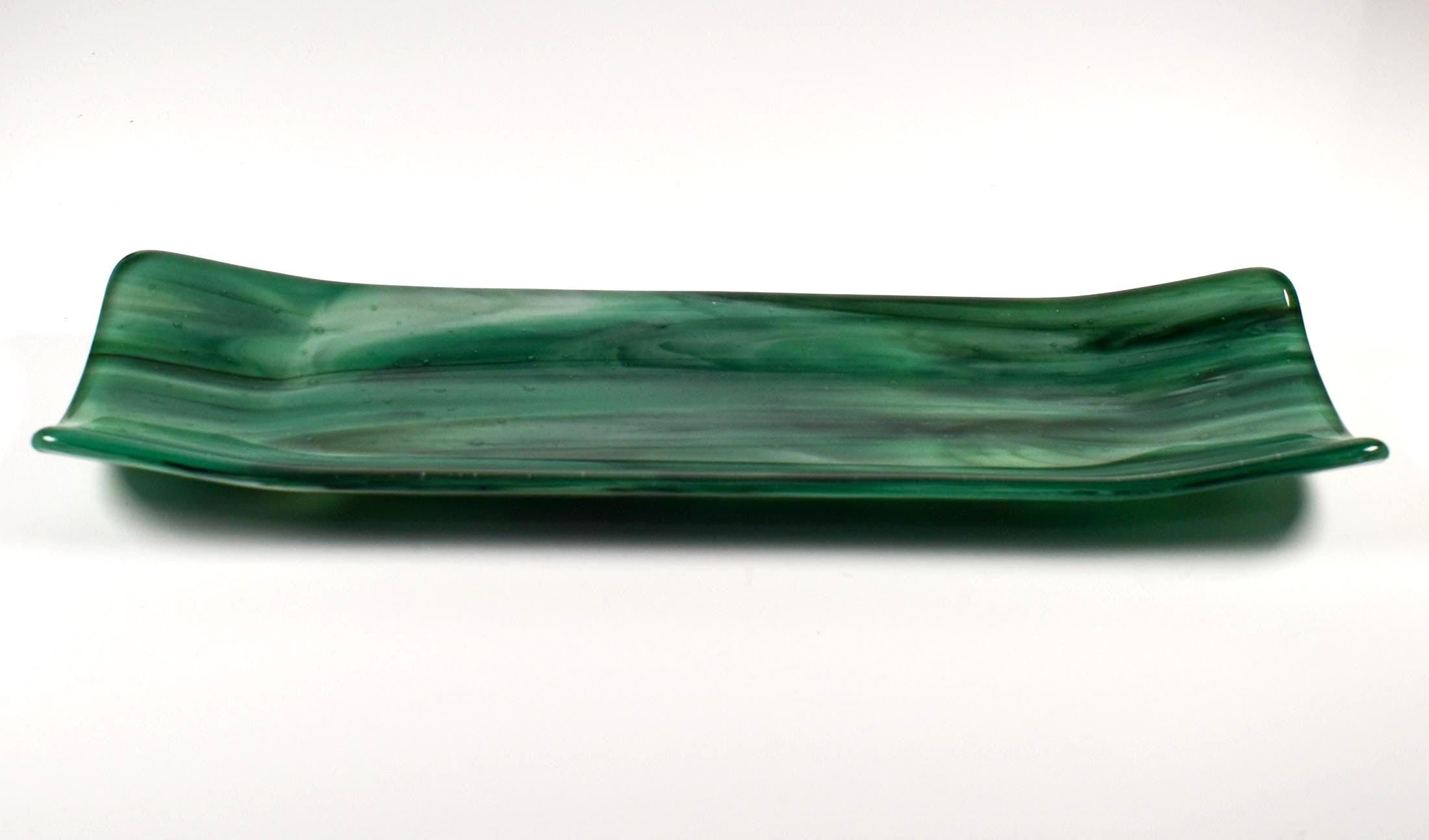Side view of an emerald green fused glass channel tray with gently upturned ends on a white background.