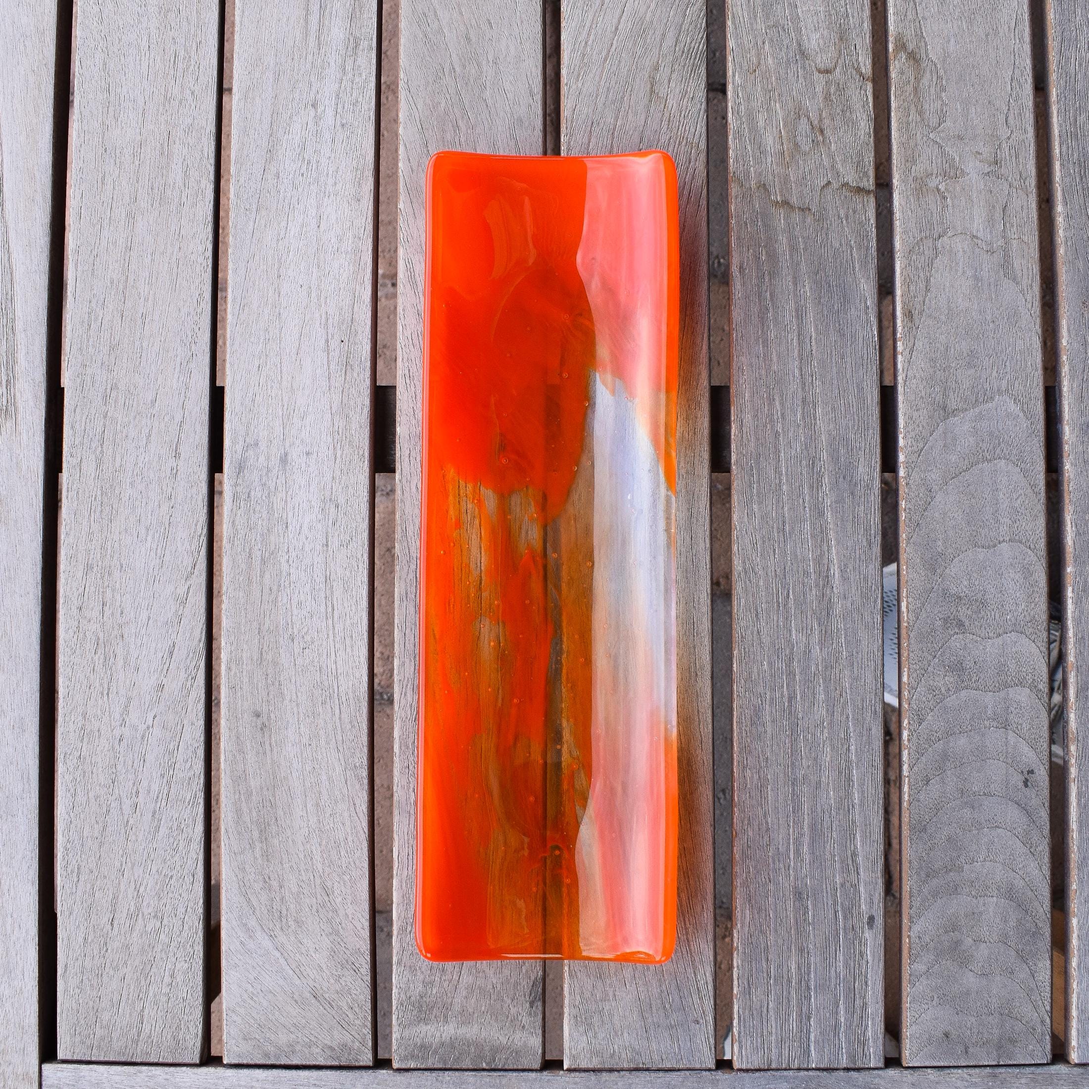 Orange and clear fused glass channel tray photographed from above a slatted wood table in natural light.