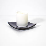 Square shaped, purple glass dish with black trim and slightly raised corners, on a white surface, holding a white jarred candle.