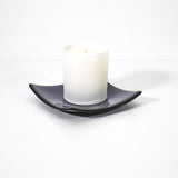 Square shaped, purple glass dish with black trim and slightly raised corners, on a white surface, holding a white jarred candle.