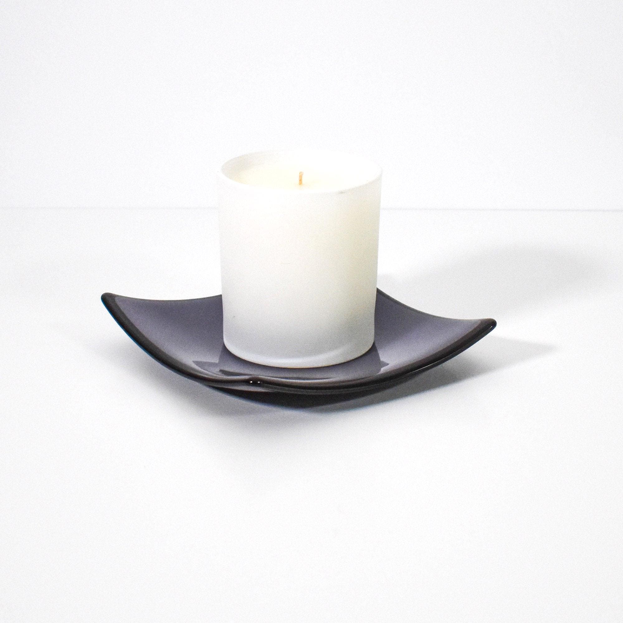 Square shaped, purple glass dish with black trim and slightly raised corners, on a white surface, holding a white jarred candle.