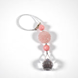 Large round carved rose quartz bead flanked by two smaller pink stone beads and anchored by round crystal prism, on white surface.