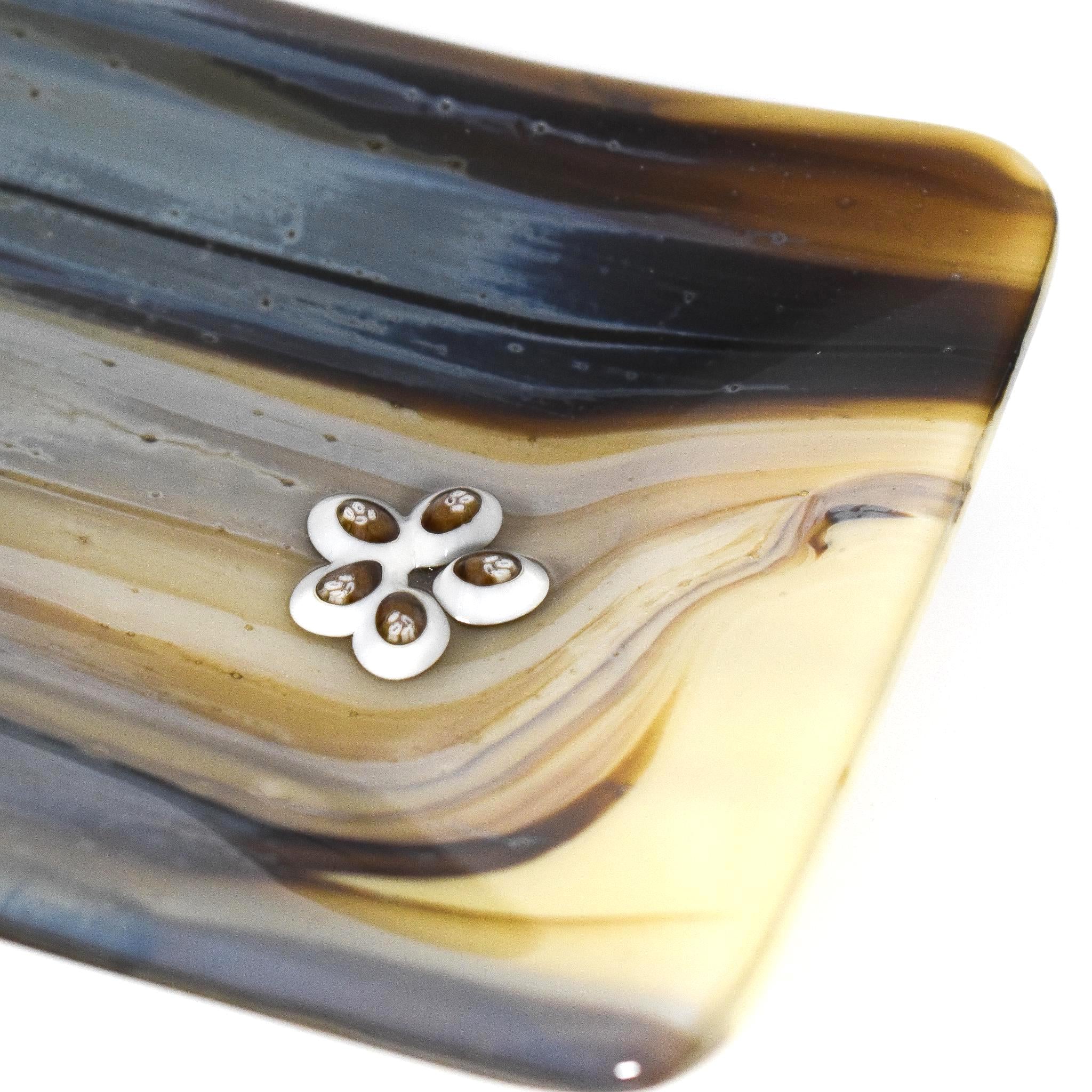 A decorative glass dish with a flower-shaped accent. The dish features a flowing pattern of brown, beige, and gray hues. The flower accent is white with brown details.