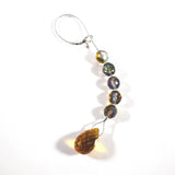 A decorative beaded ornament with a silver loop and clasp. The ornament features a string of iridescent, faceted beads in shades of purple, green, and gold, leading to a large, amber-colored teardrop-shaped crystal.
