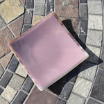 Lavender-colored square glass trinket tray on stone table.