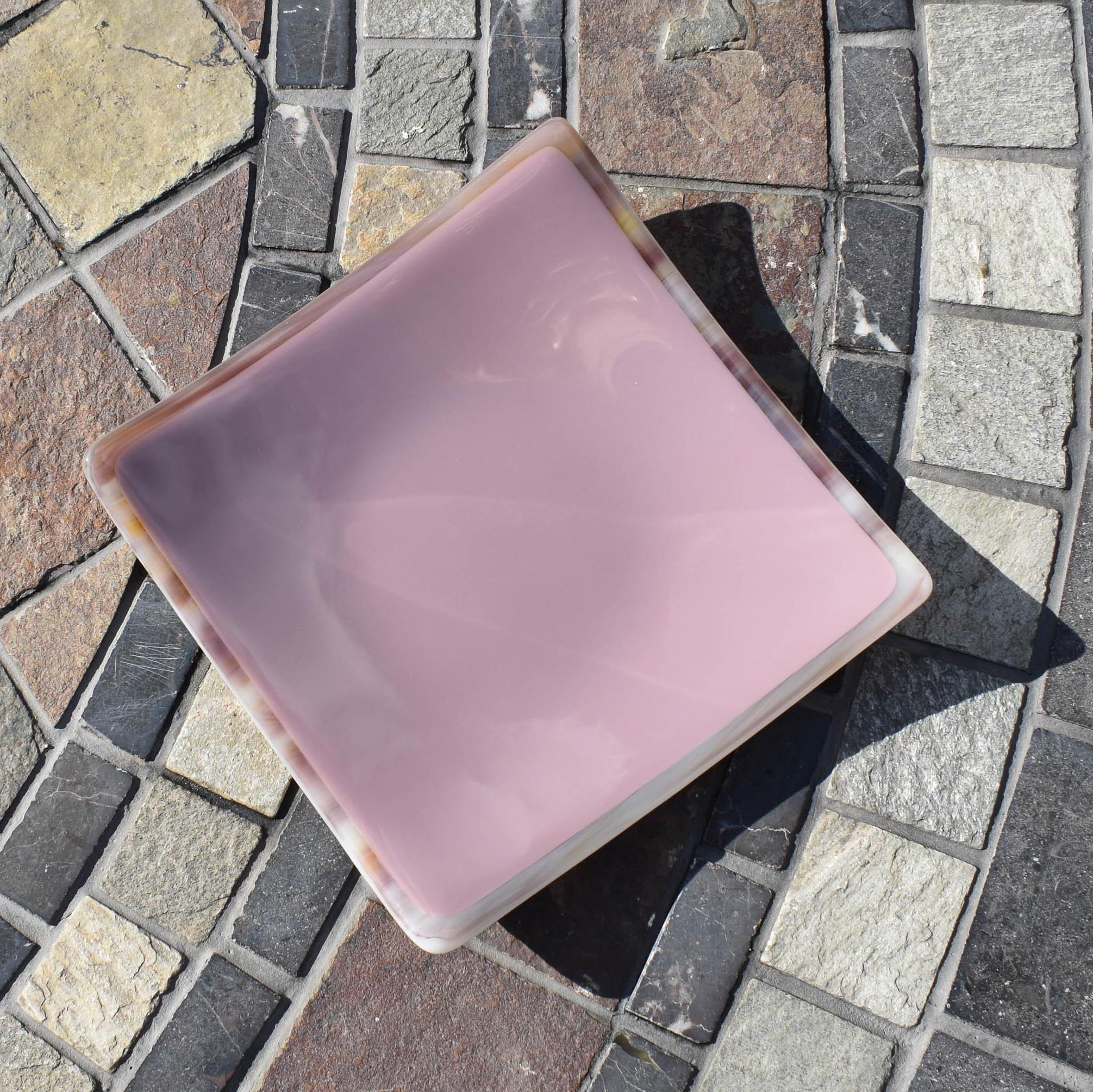 Lavender-colored square glass trinket tray on stone table.
