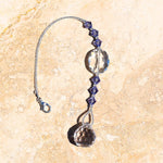 A crystal suncatcher with a silver chain and tanzanite beads. The suncatcher has a large oval crystal bead and a small, faceted crystal prism.