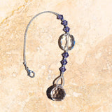 A crystal suncatcher with a silver chain and tanzanite beads. The suncatcher has a large oval crystal bead and a small, faceted crystal prism.
