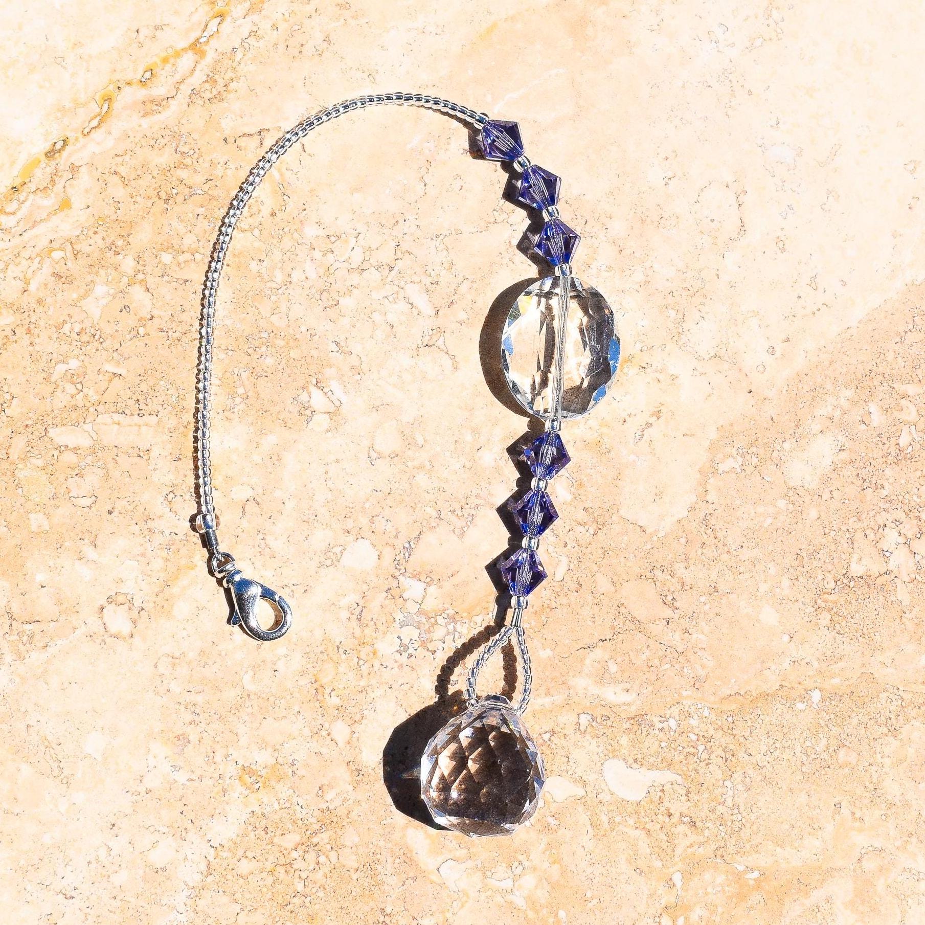 A crystal suncatcher with a silver chain and tanzanite beads. The suncatcher has a large oval crystal bead and a small, faceted crystal prism.