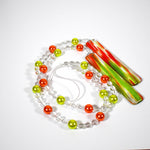 LIme green and bright orange pearl beads strung with smaller clear beads coiled on a white surface. Both ends of the wire are connected to rectangular pieces of fused glass with sparkling green and orange streaks.