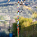 LIme green and bright orange pearl beads strung with smaller clear beads, hanging vertically from a tree, anchored by two pieces of clear/orange/green glass.