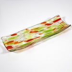 A rectangular glass serving dish with a curved design. The dish features a clear base with green and orange abstract patterns. The colors are swirled and speckled throughout the glass, creating a unique and artistic look. The edges are slightly raised.