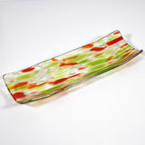 A rectangular glass serving dish with a curved design. The dish features a clear base with green and orange abstract patterns. The colors are swirled and speckled throughout the glass, creating a unique and artistic look. The edges are slightly raised.