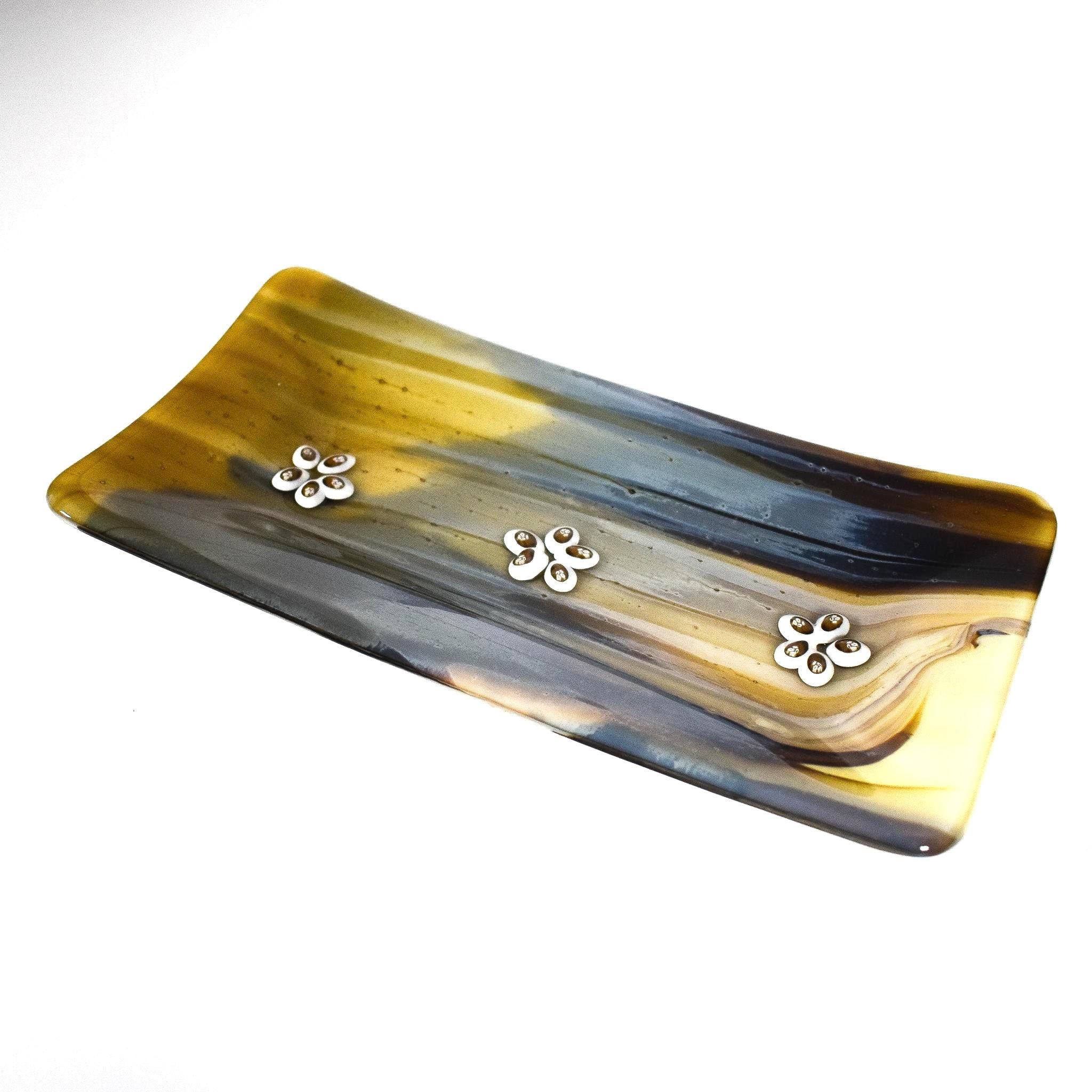 A rectangular glass serving tray with a yellow, brown, and gray marbled design. The tray has three silver flower-shaped embellishments.