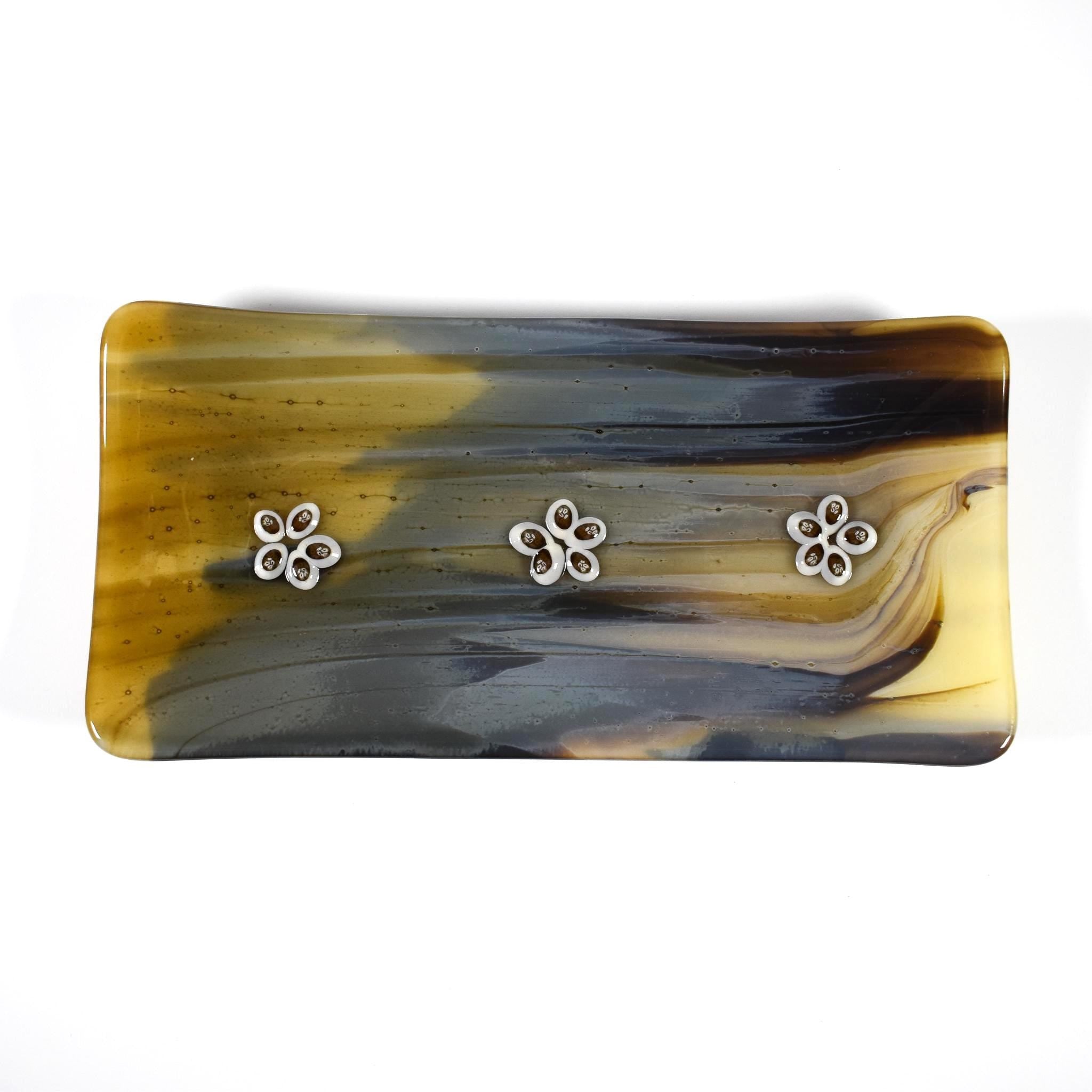 A rectangular glass dish with a marbled design in shades of gold, brown, and gray. Three small flower accents are evenly spaced across the top surface.