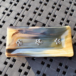 A rectangular glass dish with a marbled pattern in shades of tan, brown, and gray. Three small, white flower-shaped embellishments are evenly spaced across the top.