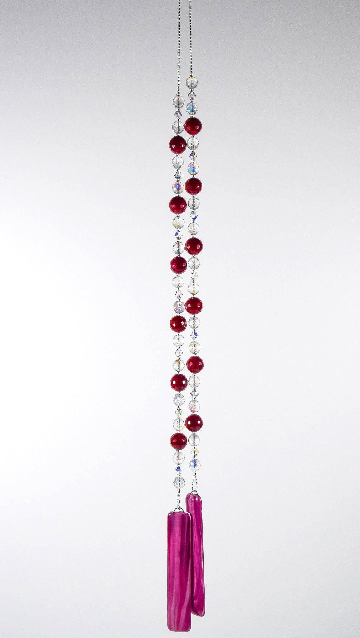 Large cranberry red jade stones beaded with glass and crystals, anchored by two pieces of dark cranberry pink fused glass, hanging vertically against white background.