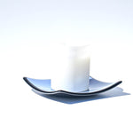 A white frosted glass candle holder with a blue and black wavy glass saucer.