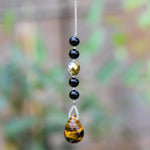 A gold and black beaded car charm with a teardrop-shaped tiger's eye gemstone pendant.