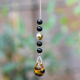 A gold and black beaded car charm with a teardrop-shaped tiger's eye gemstone pendant.
