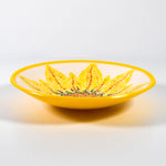 Round fused glass bowl with hand-painted sunflower design and bright yellow trim on white surface.