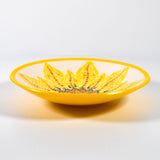 Round fused glass bowl with hand-painted sunflower design and bright yellow trim on white surface.
