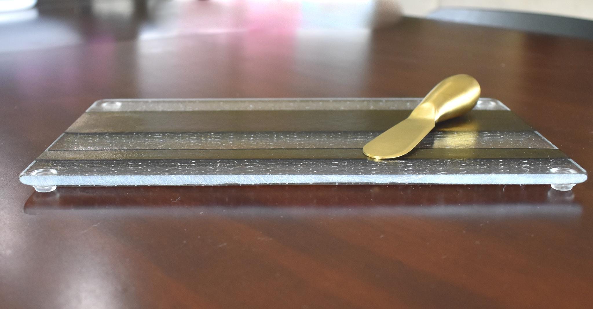 A clear glass cheese board with a gold-toned design and a gold-colored cheese knife.