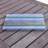 A clear glass cutting board with a striped design in gold and black. The board is sitting on a wooden surface.