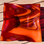 Large square glass bowl with wavy edges and a square center foot, viewed from above sitting on a slatted wood table, outside in sun light.